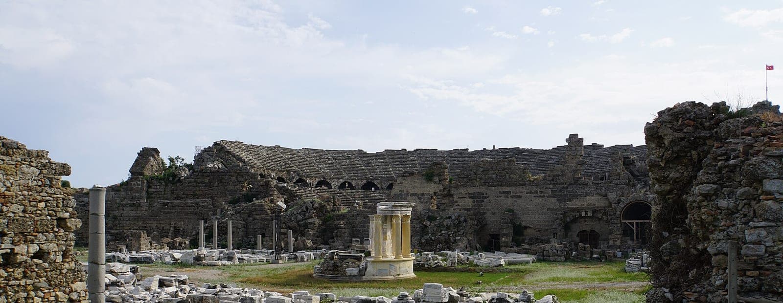 Die Außenmauer des römischen Theaters von Side, davor ein Rundbau zwischen den Fundstücken.